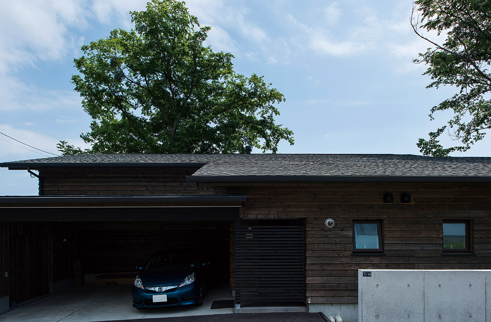 傾斜地を生かした建物は、玄関側から見ると平屋造りのよう。屋根越しにそびえるのは、庭のシンボル、ハルニレの巨木