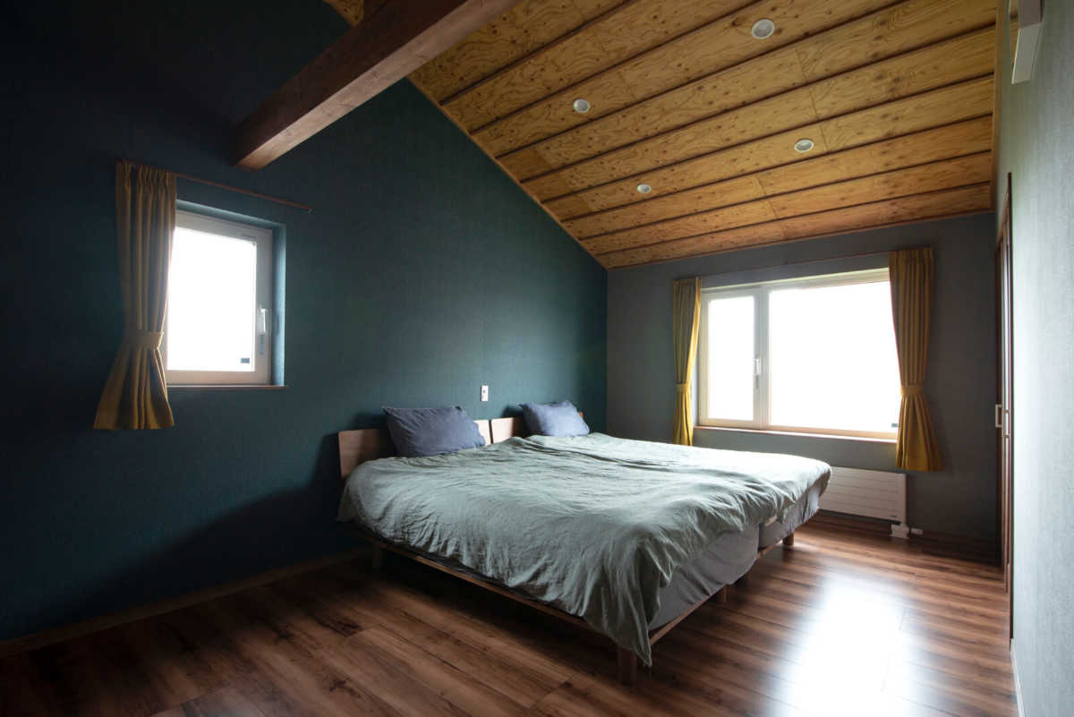 2階の寝室は屋根形状を活かした斜め天井に。ぬくもりある木張りと深いグリーンの壁が落ち着きをもたらす