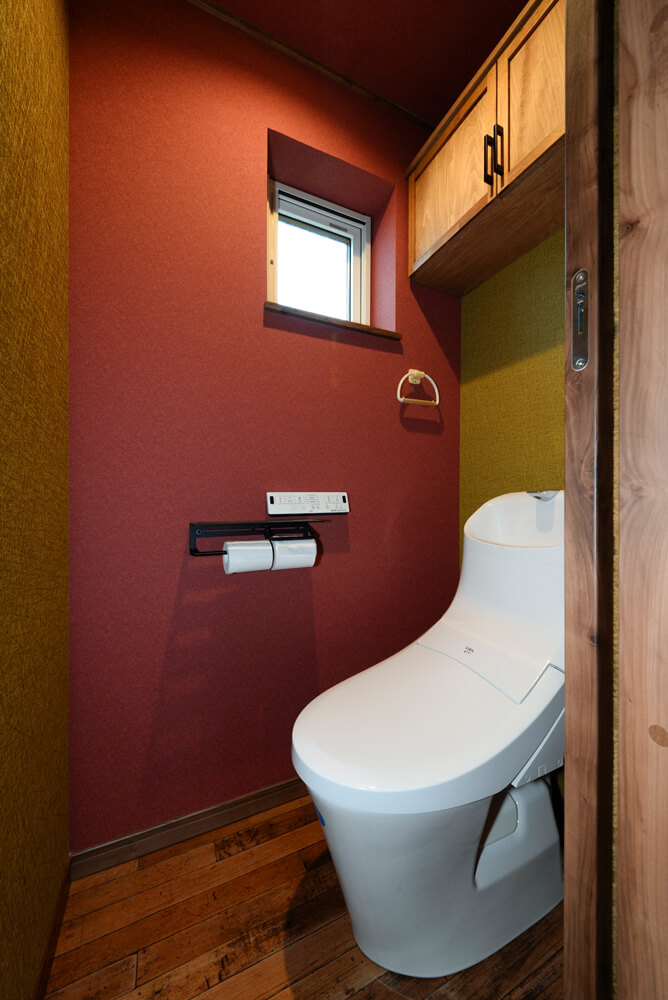 遊び心を持たせたトイレのデザイン。べんがら色のアクセントクロスが和モダンな印象を与える