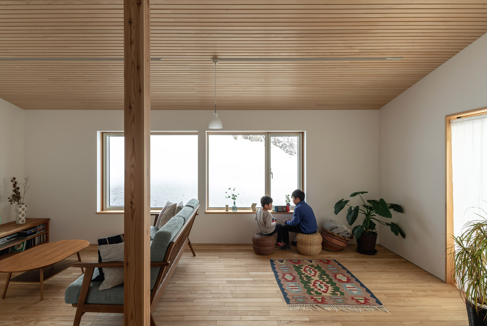 カラマツを用いた親柱がオープンな空間のアクセントに。1階の床は、ご夫妻がオイルステインで仕上げたタモ無垢材。右の木製引き戸の向こうは道南スギで設えたデッキ。玄関脇に設えた奥さんのアトリエが目隠しになり、夏季にセカンドリビングとなる