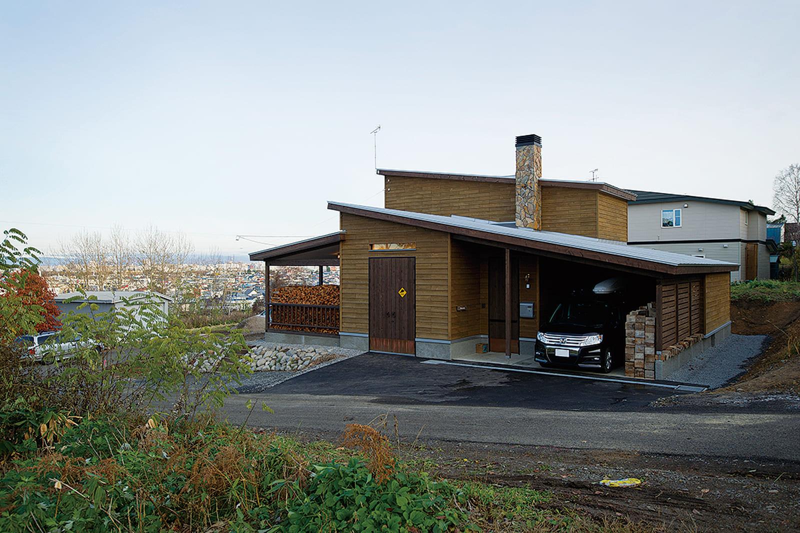 片流れの屋根に煙突、薪かが積まれたデッキや道南スギの外壁と、山小屋風の佇まいが印象的なOさん宅