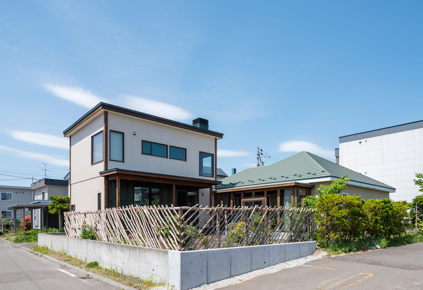 2棟の建物がさりげなく調和するNさんご一家の住まい。手前の木の塀は直接伐採してきてつくったお手製のもの