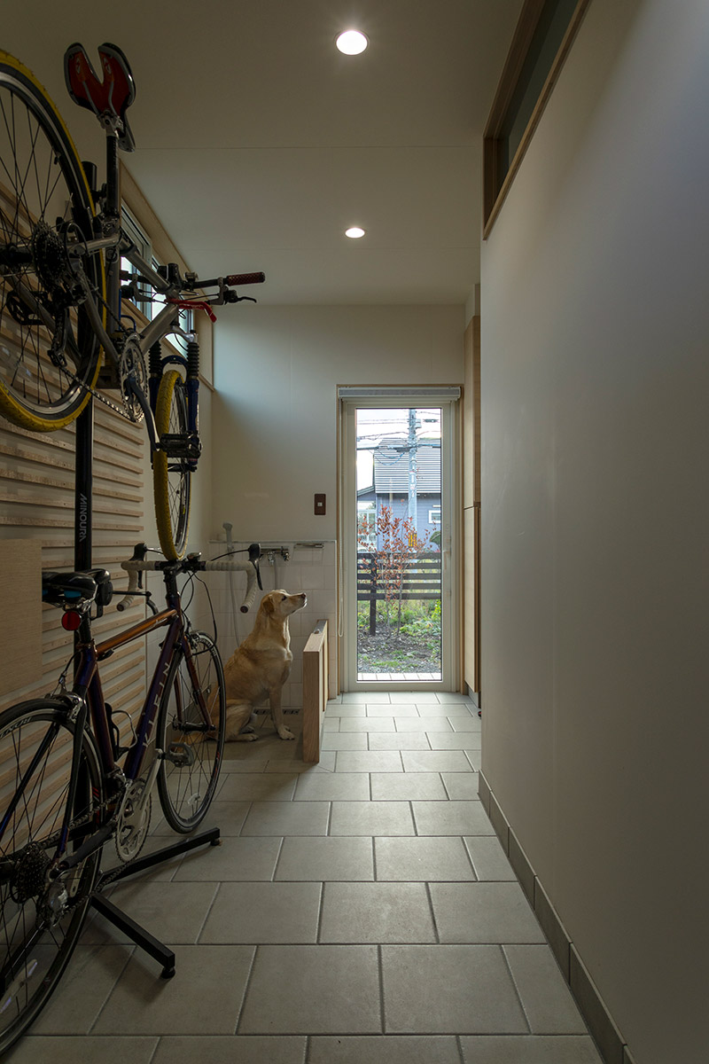 Sさん愛用の自転車と、ギンくん専用の洗い場を設けた広い玄関ホール。突き当たりには庭へ抜ける出入り口を設け、正面玄関と合わせて、ギンくんとの散歩時はどちらからも出入りができる
