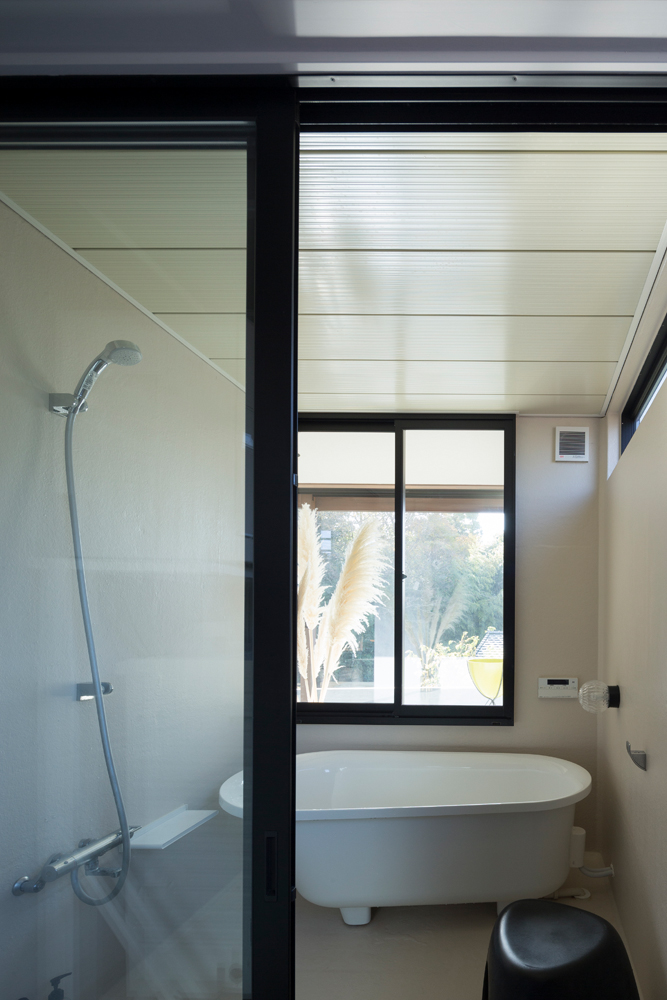 白い置型バスタブと黒い窓枠の組み合わせがスタイリッシュな浴室。大きめな窓からは、半屋外テラスを介して近くの森の木々が眺められる