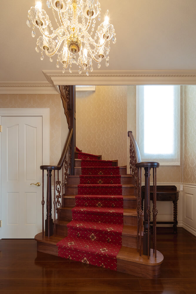 玄関ホールから美しいアールを描いて2階へ続く階段。天井のシャープなモールや手すりの滑らかなカーブもまた、匠の技によるもの