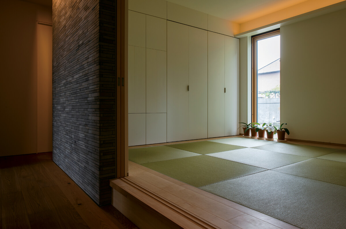 玄関ホールの石タイルを採用した壁の奥は、利休畳とカバの板畳がモダンな和室。さまざまな素材が美しいハーモニーを奏でる