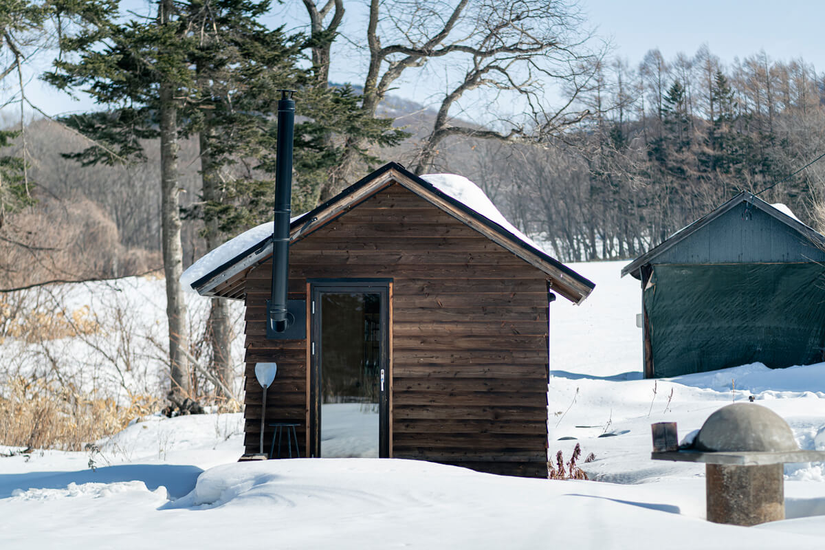 小屋の屋根の形状は、もともと敷地内に建っていた三角屋根の車庫（写真右奥）に合わせてデザイン。出入り口のドアは、全面ガラスで窓のような機能も兼ねる