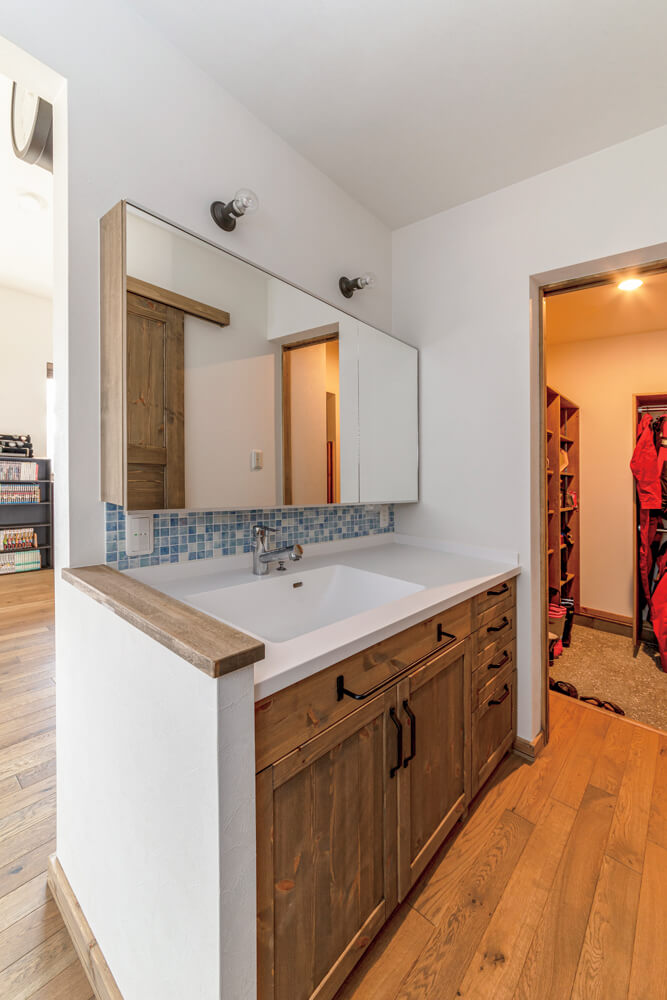 造作スウィングドアを設けたシューズルームは水まわり、パントリー、キッチンへと動線がつながっている。シューズルームの隣は、洗面スペース。木製扉やタイルが可愛い洗面台も造作仕様