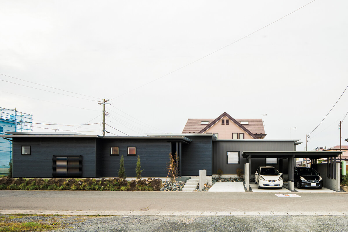 焼きスギ材とダークグレーのガルバリウム鋼板がシックな外観。旧家の庭石を石垣として残し、思い出を引き寄せるよすがに