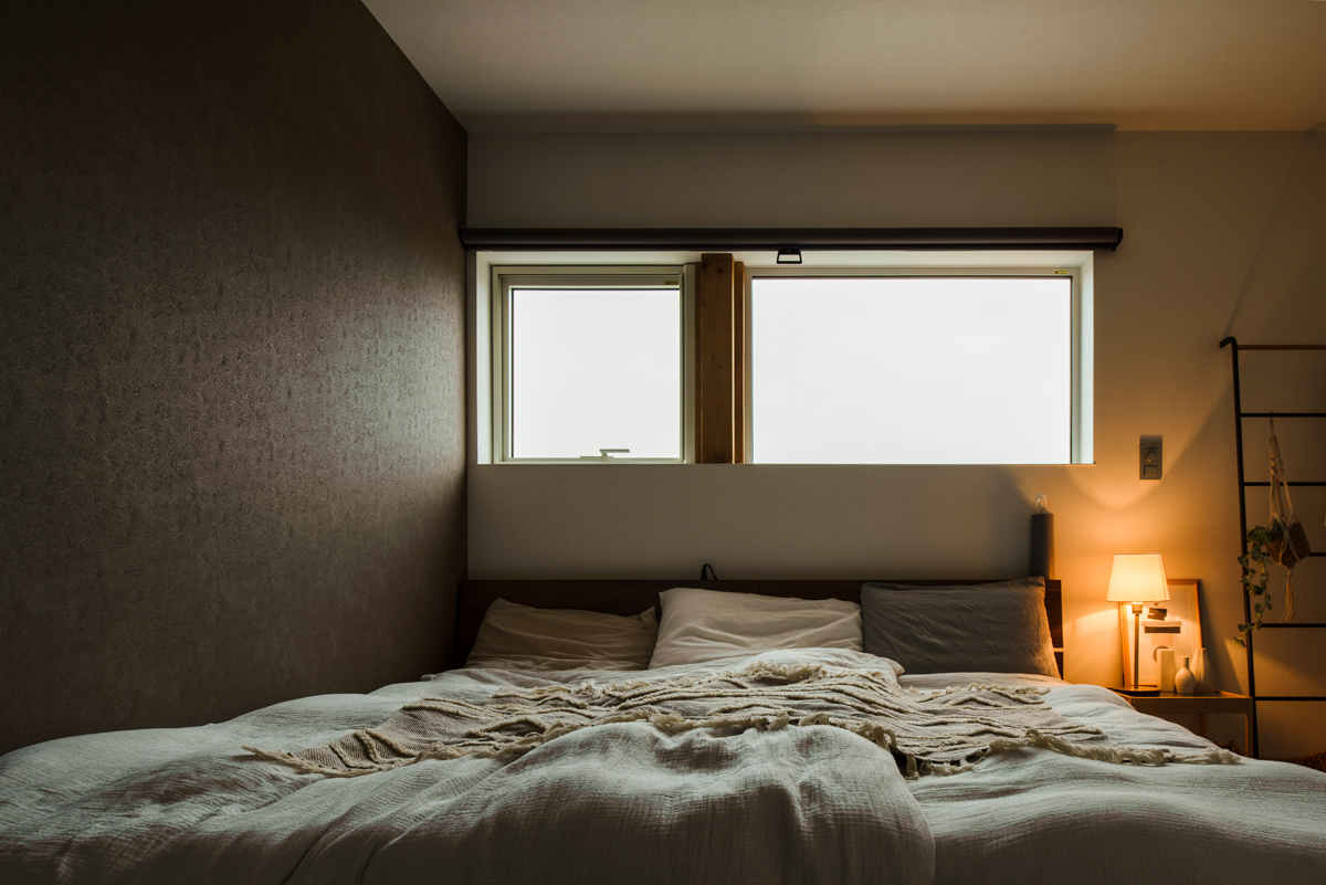 ナチュラルな色と素材感でコーディネートしたリラクシングな寝室。ダークブラウン色のアクセントウォールが空間を引き締める
