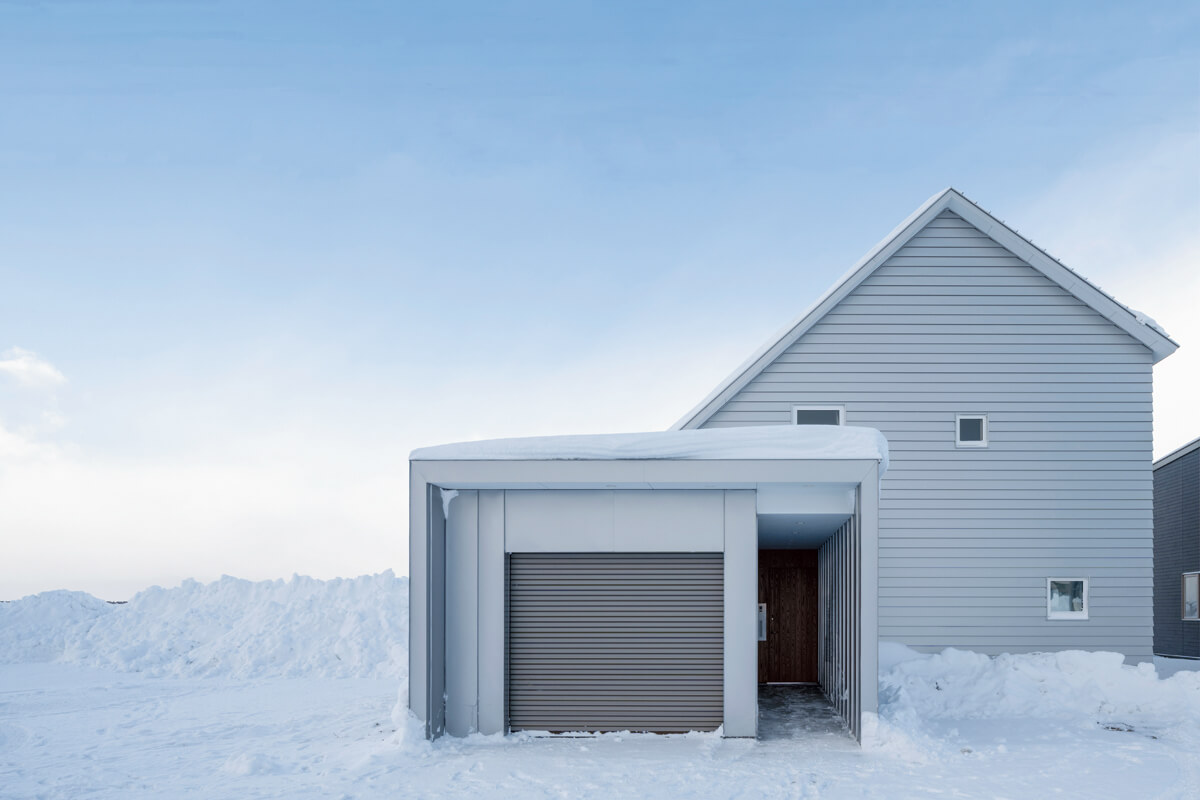 清廉な冬景色に調和する白いガルバリウム鋼板仕上げの外観。ガレージと屋内は直接行き来できる