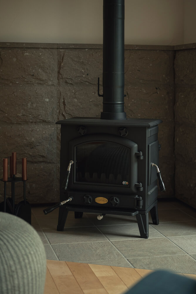 薪ストーブは補助暖房なので、あえてコンパクトなモデルを選んだ。炉壁には札幌軟石を使い、グレーの石調タイルを合わせスタイリッシュに
