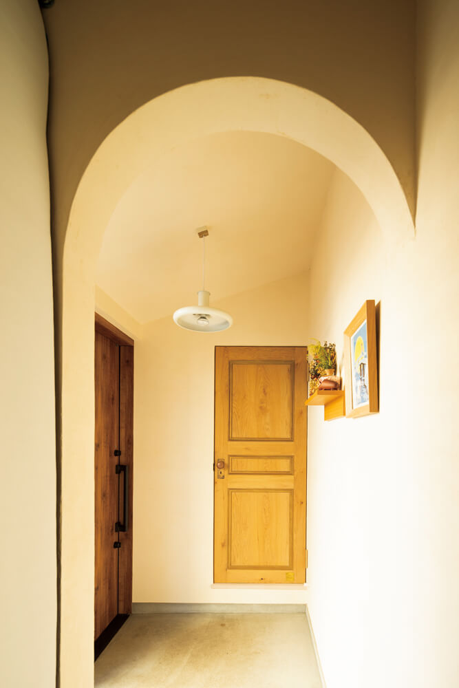 玄関とLDKをつなぐのは造作したドア。Kさんご夫妻が自ら探したアンティークのドアノブの雰囲気に合うデザインに仕上げた。玄関土間と玄関収納を仕切るアールの下がり壁が空間のアクセントに