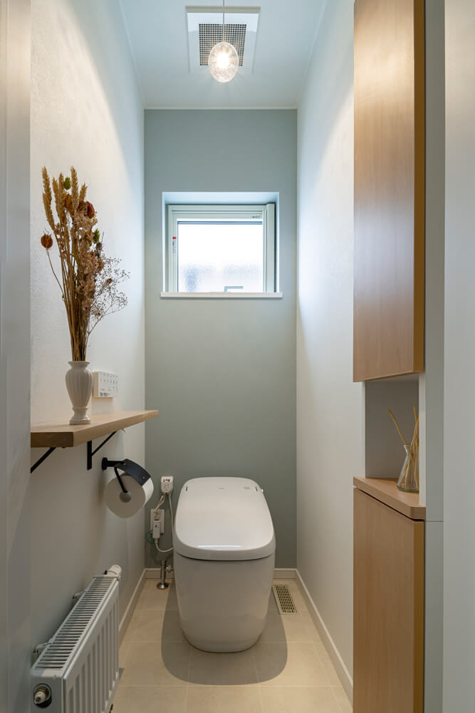 採光窓を設けた明るい1階トイレ。ブルーグレーのアクセントウォールとタモ材の造作が優しいアクセントになっている