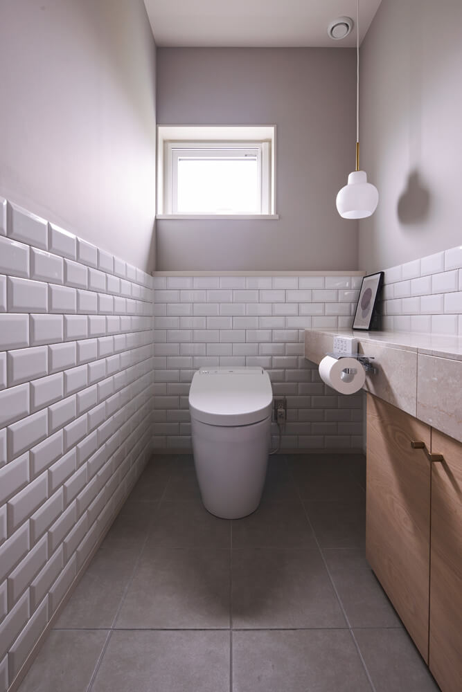 淡いグレーと白を基調にしたトイレには、サブウェイタイルをあしらった。照明は、ルイスポールセンのVLリングクラウン