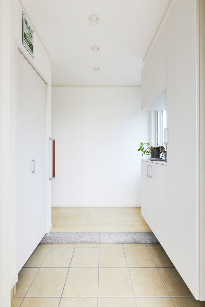 白を基調にし、床も明るい色調の屋内。左側に大容量の収納スペースがあり、玄関が乱雑にならない
