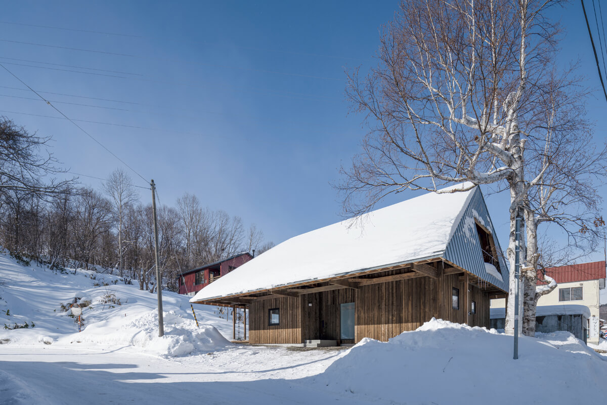 斜面から連なるように配置された大屋根の家。冬は太陽の光が雪の斜面に反射し、室内やテラスを明るく照らす