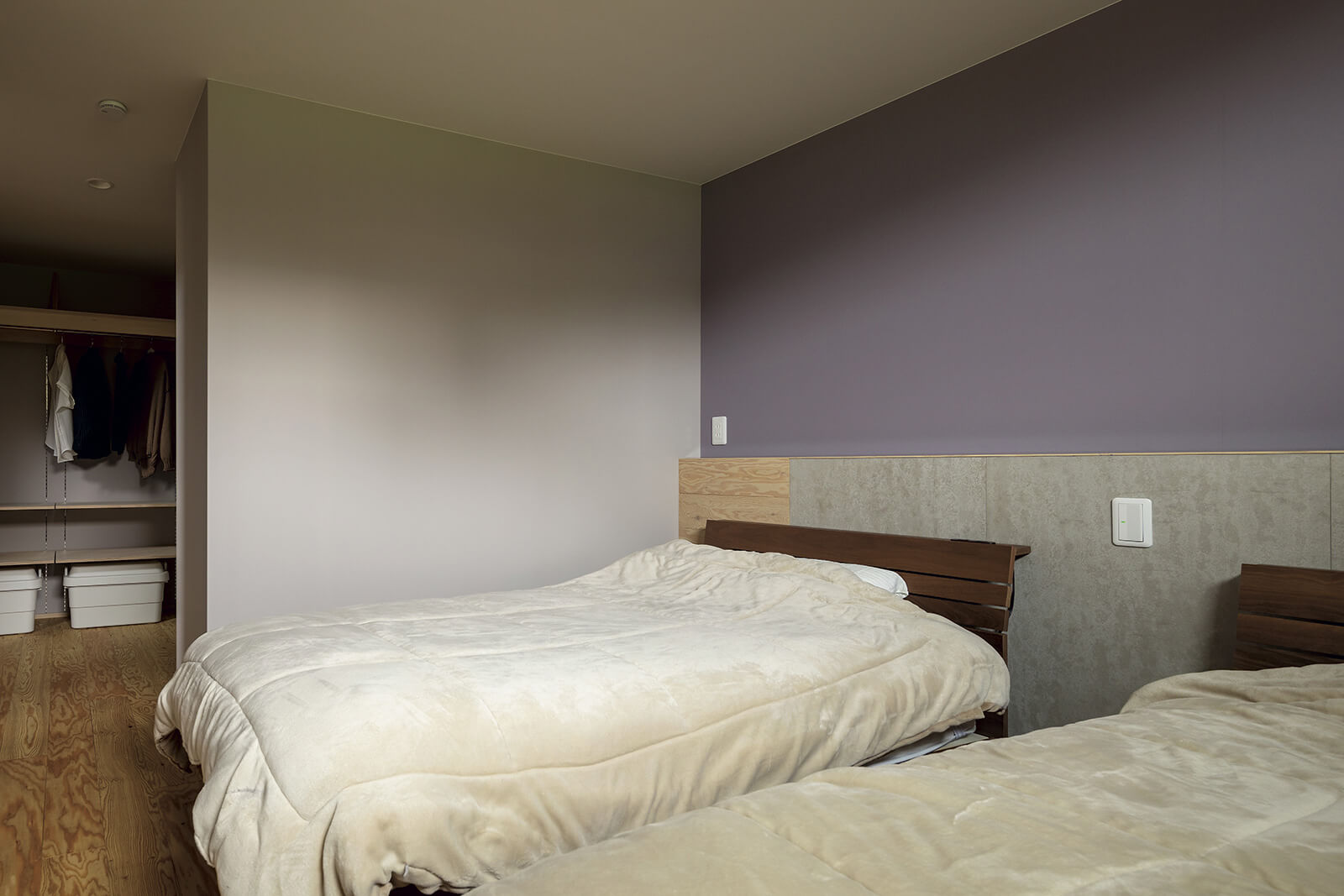 大容量のウォークインクローゼットを備えた寝室。淡い紫のアクセントウォールが、シンプルな空間にやわらかな表情を与える