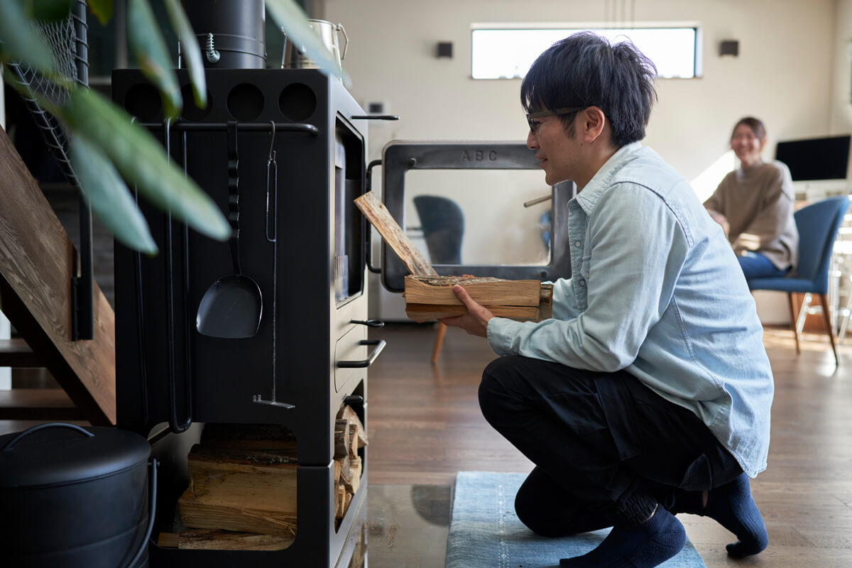 「薪ストーブをつけること、それ自体が大きな楽しみになっています」と薪をくべるMさんを奥さんが笑顔で見守る