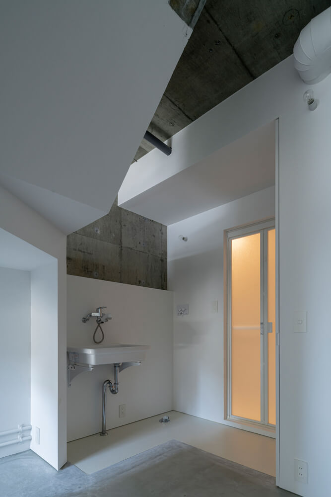 階段下の洗面と浴室。壁や床は水まわりスペースを境界線に素材が変化する