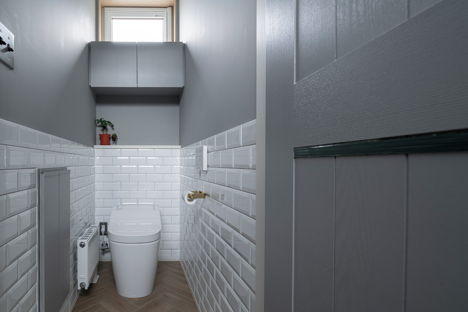 グレーのペイントに白いサブウェイタイルを合わせたトイレ。ヘリンボーン柄に施工した床タイルと真鍮のホルダーでインダストリアルな雰囲気に