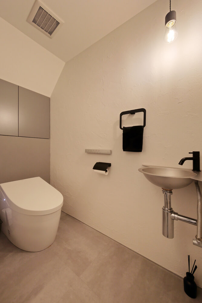 モダン＆シックなテイストで仕上げたトイレは、壁面収納と手洗い器を備えている