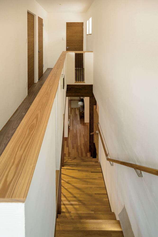 櫛引き仕上げの塗り壁とナラの床板、アイアン柵が美しい調和を見せる階段。正面は子ども部屋