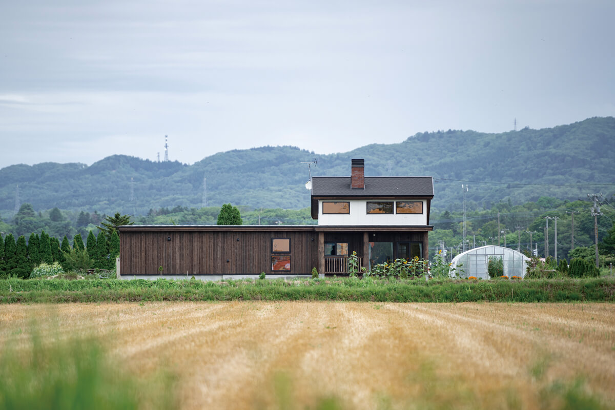 広大な田園風景の中で、道南スギを使った木張りの外観と煙突がひときわ目を引くMさん宅