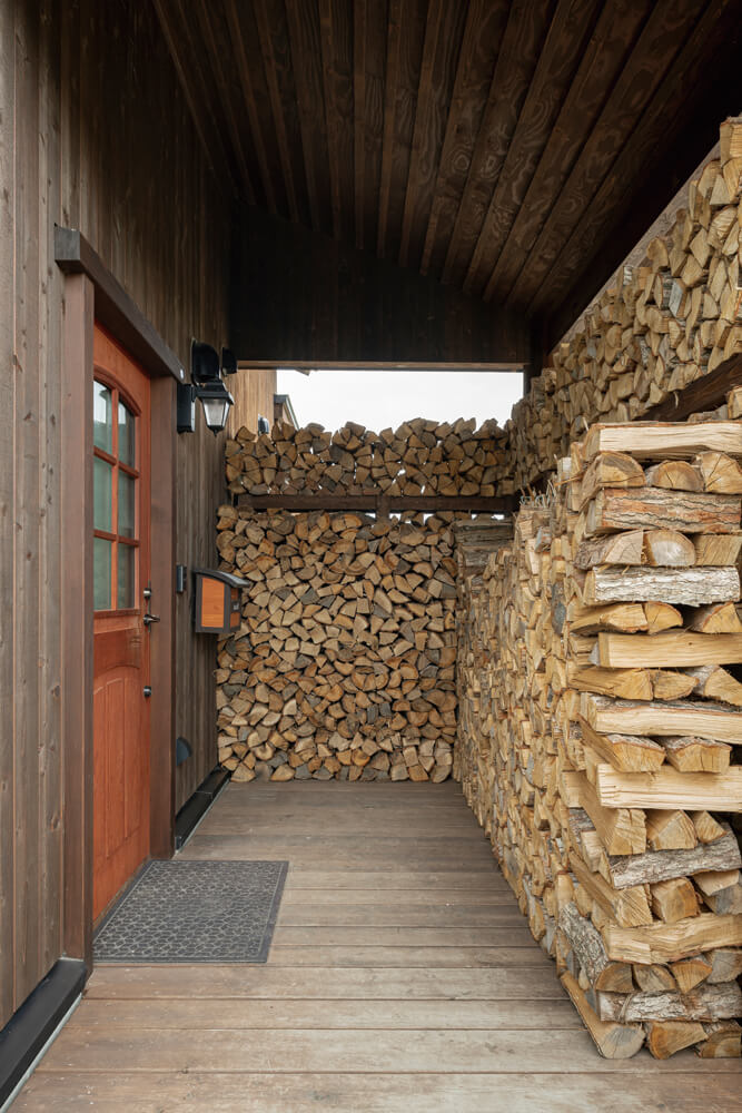 玄関の屋根下に設けた薪棚は、風や雪除けも兼ねている。精緻に積まれた薪の佇まいも美しい
