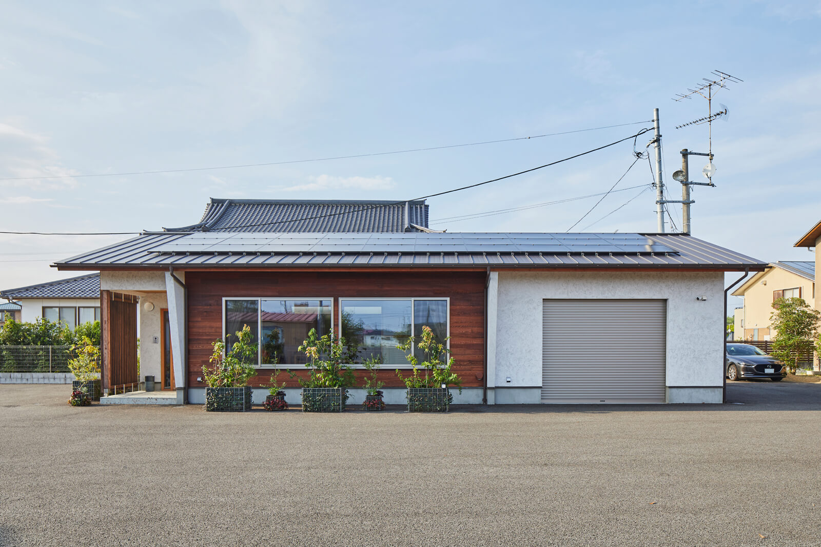 メンテナンスフリーのそとん壁を採用した切妻屋根の平屋。ファサードの一部にレンガ色に着色したレッドシダーを施工した。どっしりとした佇まいは平屋ならでは