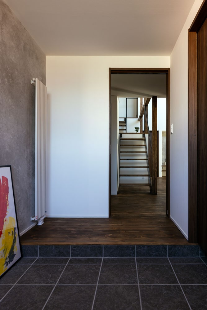 グレイッシュな色合いに整えた漆喰のアクセントウォールを採用した玄関ホール。動線はリビング、階段へそのままつながっている