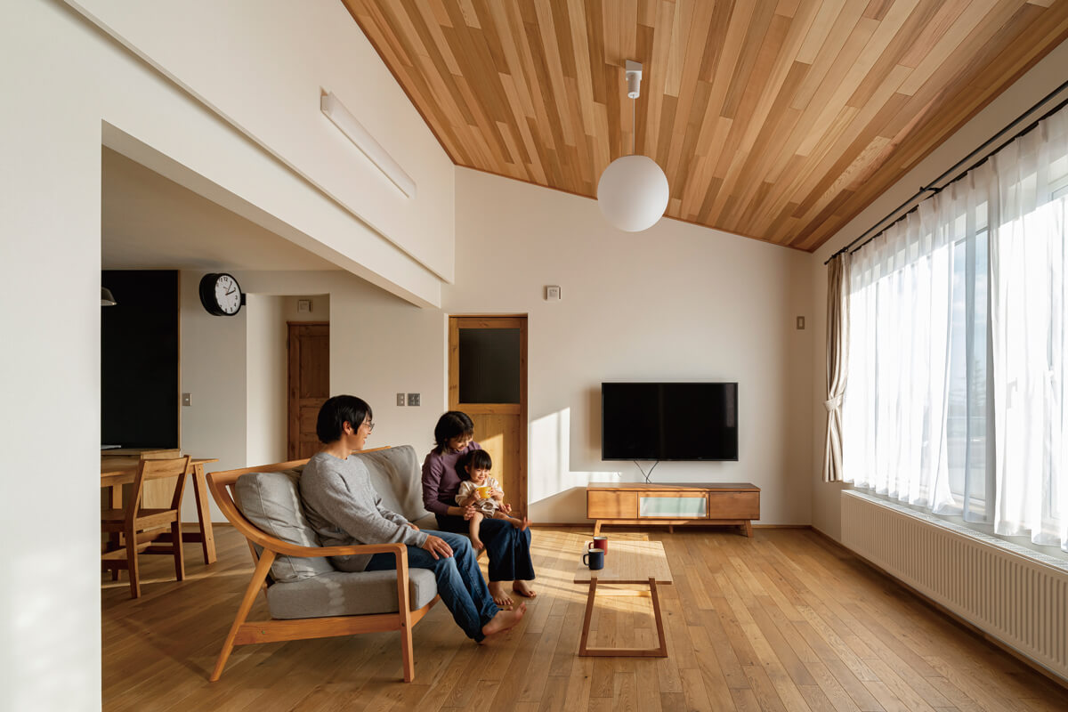 レッドシダーを張った屋根なり天井が心地よい広がりをつくり出すリビング。壁付けテレビの下の収納は造作。家具も、木質感あふれる室内の雰囲気に合わせて選んだ