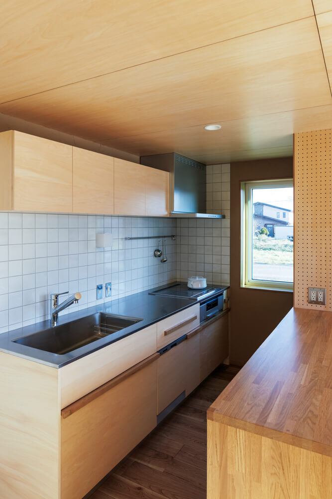 造作のキッチンは壁付けでレイアウト。木を基調とした空間の見た目の気持ちよさを保つため、冷蔵庫が見えないように置き場所を工夫した