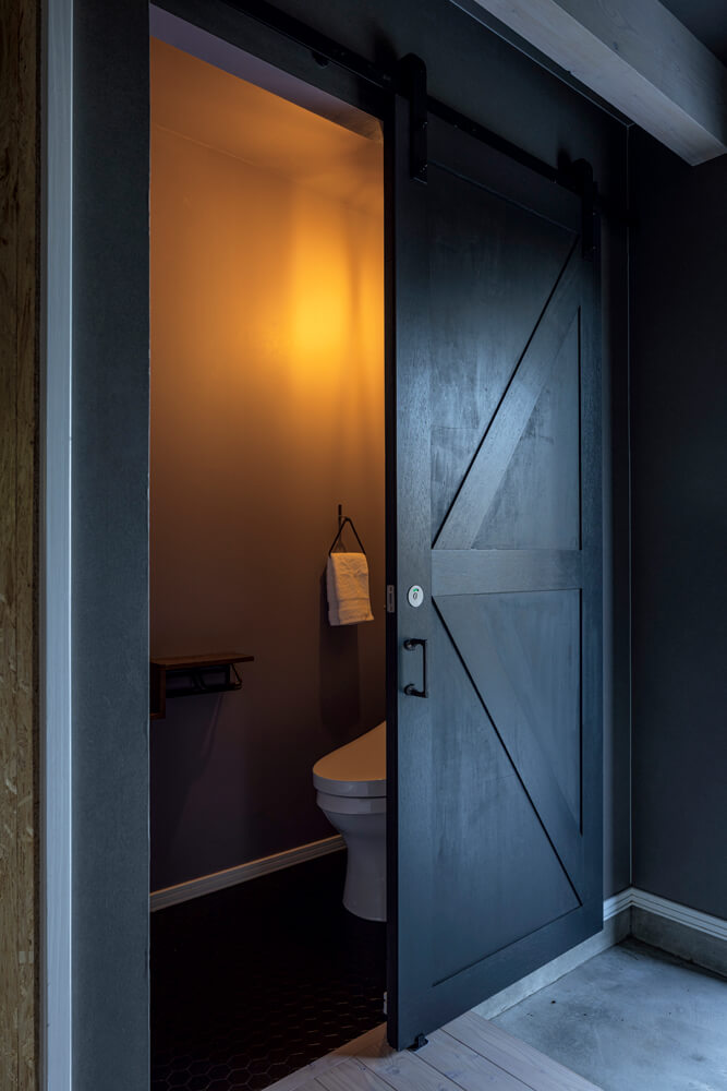 玄関ホールに隣接するトイレ。壁のように見える木製造作吊り引き戸を採用