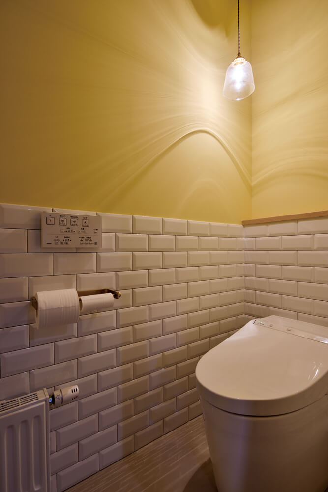 トイレはイエローと洗面台と同じサブウェイタイルの組み合わせに。トイレットペーパーホルダーは真鍮製を採用した