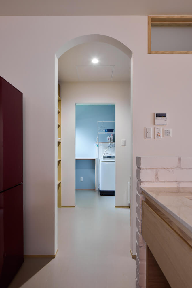 キッチンとブルーにペイントしたユーティリティは洗面台を介して直線で結ばれている。アール型の出入り口がやわらかな雰囲気を演出