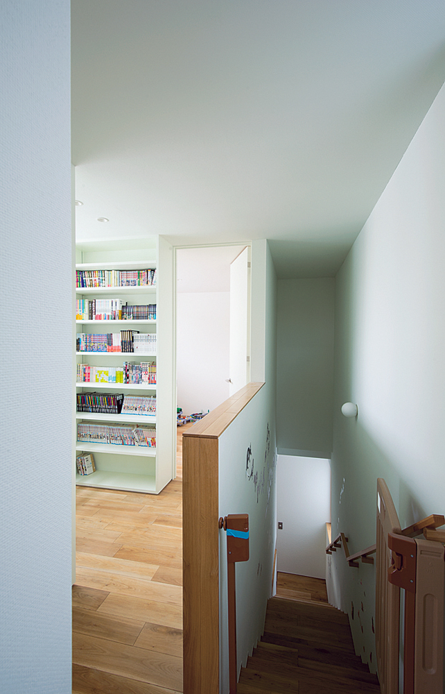 キッチン裏の階段でつなぐ2階は、個室を配した完全プライベート空間。吹き抜けに面したスペースには本棚を造作