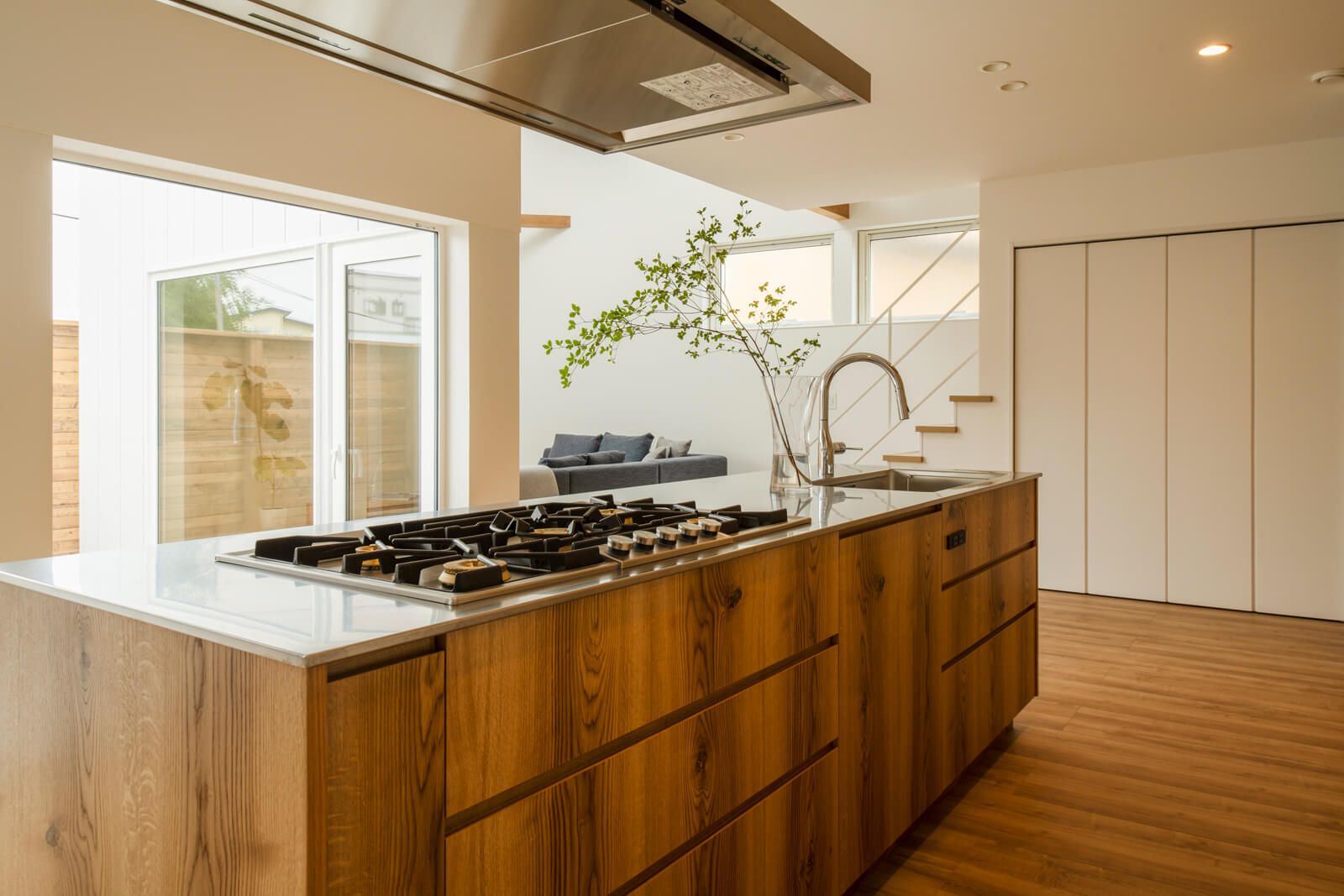 オールステンレスの天板と木の面材が美しく調和しているフルオープンのアイランドキッチンと、斜めにずらして配置したリビングは程よい距離感