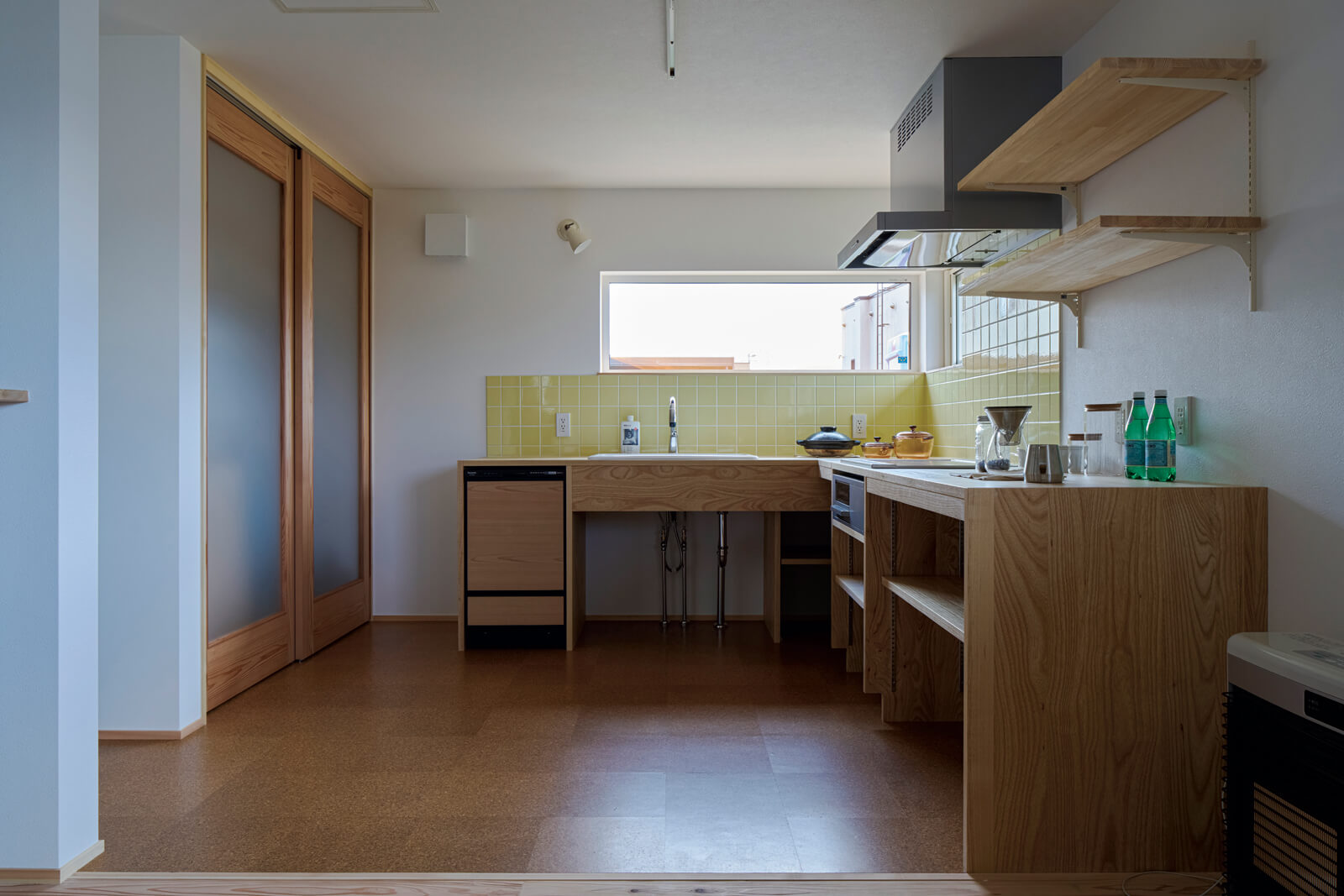 パントリーを備えたキッチンは壁付け・L字型に造作することで、省スペースと家事効率の向上を実現。床には耐水性に優れ、足触りの良いコルクタイルを採用した。窓を配することで視線が抜け、壁付けの圧迫感が軽減