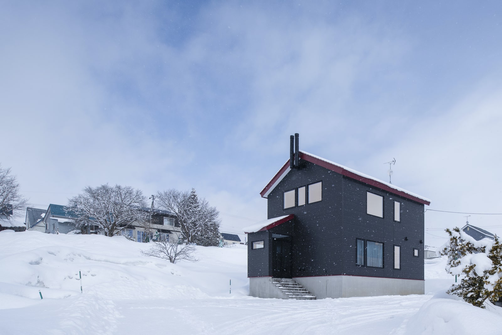 雪対策のために、基礎高にしたMさんご一家の住まい。Mさんの好きな赤を採用した三角屋根が雪景色に映える。床下から給気した新鮮な空気は、室内をくまなく暖めたのち、2本の排気筒から排気される