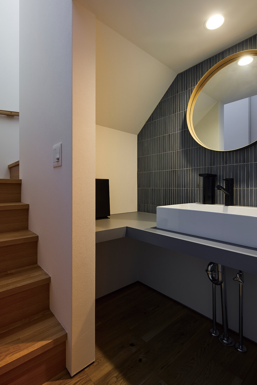 階段下のデッドスペースを利用した手洗いコーナー。黒のタイルと丸鏡がホテルのようなラグジュアリー感を演出
