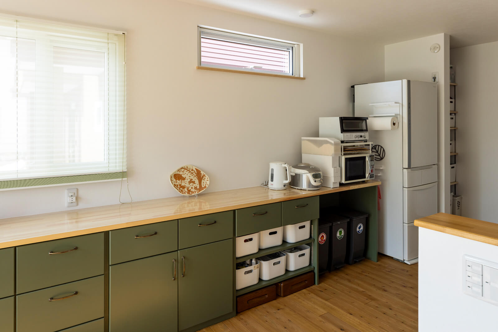 渋いグリーンの面材を用いたキッチンの背面収納は造作仕様。冷蔵庫の横には造作棚を設け、収納力抜群。買い置き食材の整理もしやすい