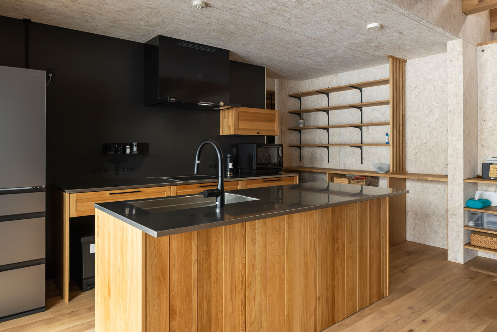 黒と木でコーディネートしたWOODONEのキッチン。IHクッキングヒーター前の壁はAさんの要望で、マグネットが使えてメンテナンスもしやすいガルバリウム鋼板で仕上げた