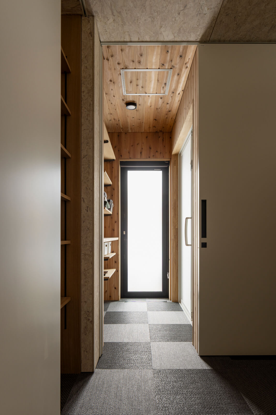 壁一面にオープン収納棚を設えた脱衣室。床には素足に心地よいスウェーデン生まれの織物床タイル「ボロン」を採用した。突き当たりのドアからは、庭やテラスにアクセスできる