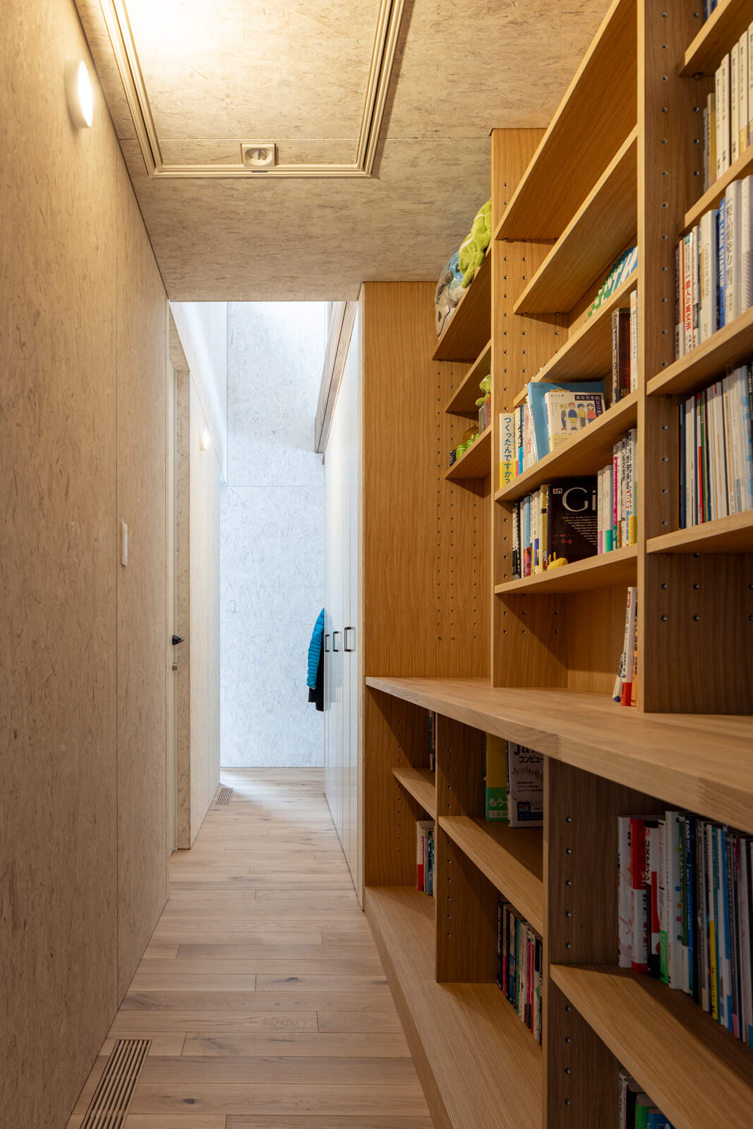 水まわりから個室、玄関土間へとつながる裏動線。LDKとの間仕切りを兼ねる壁には本棚や収納スペースを造作。天井にはロフト収納用の折りたたみ式のはしごが組み込まれている