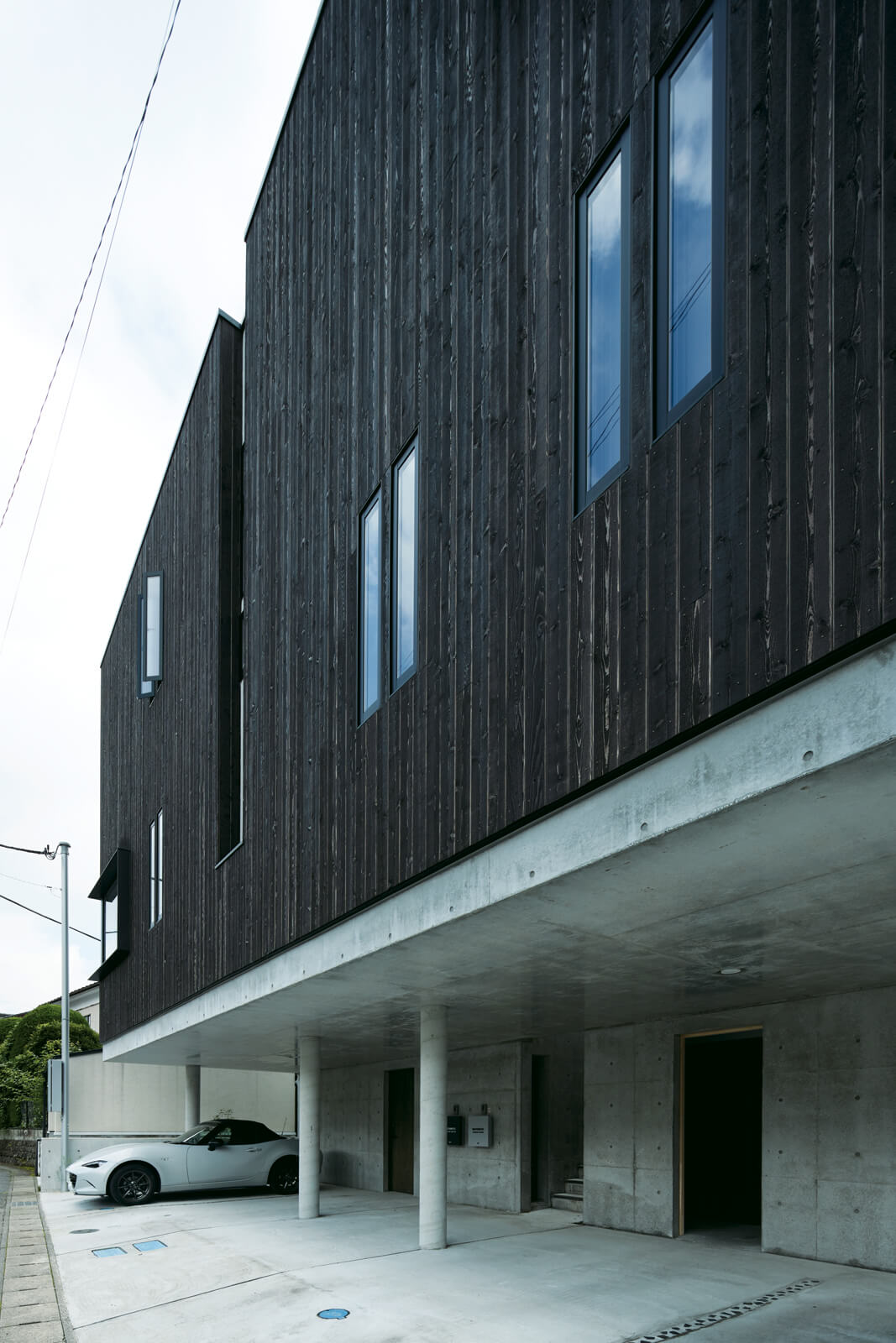 多世代がさまざまな形で暮らす周辺環境に合わせ、外観は暗めに彩色したレッドシダーとコンクリートでスタイリッシュに仕上げた