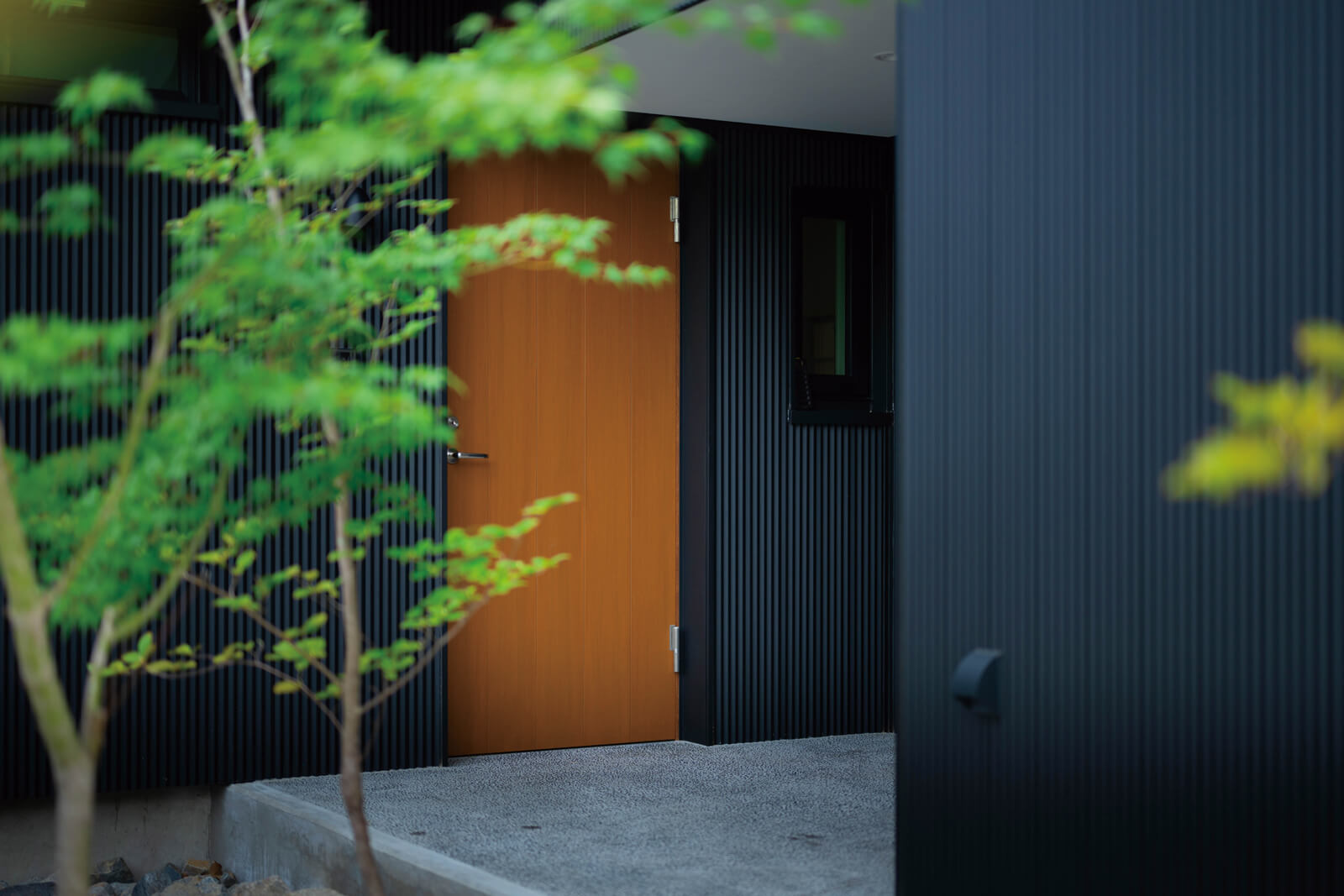 玄関ドアはスウェーデン製の木製ドアを採用。黒い壁に赤めの木の色が映える
