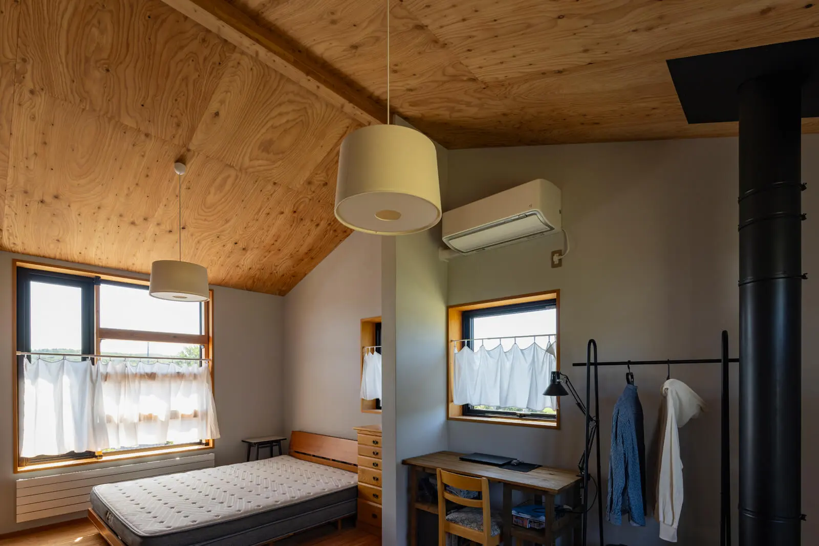 カラマツの屋根なり勾配天井の寝室。Hさんの書斎としても活用できるよう、窓にはデスクも備えた。冬は開口からの陽射しと薪ストーブの煙突から伝わる熱が空間を優しく暖める