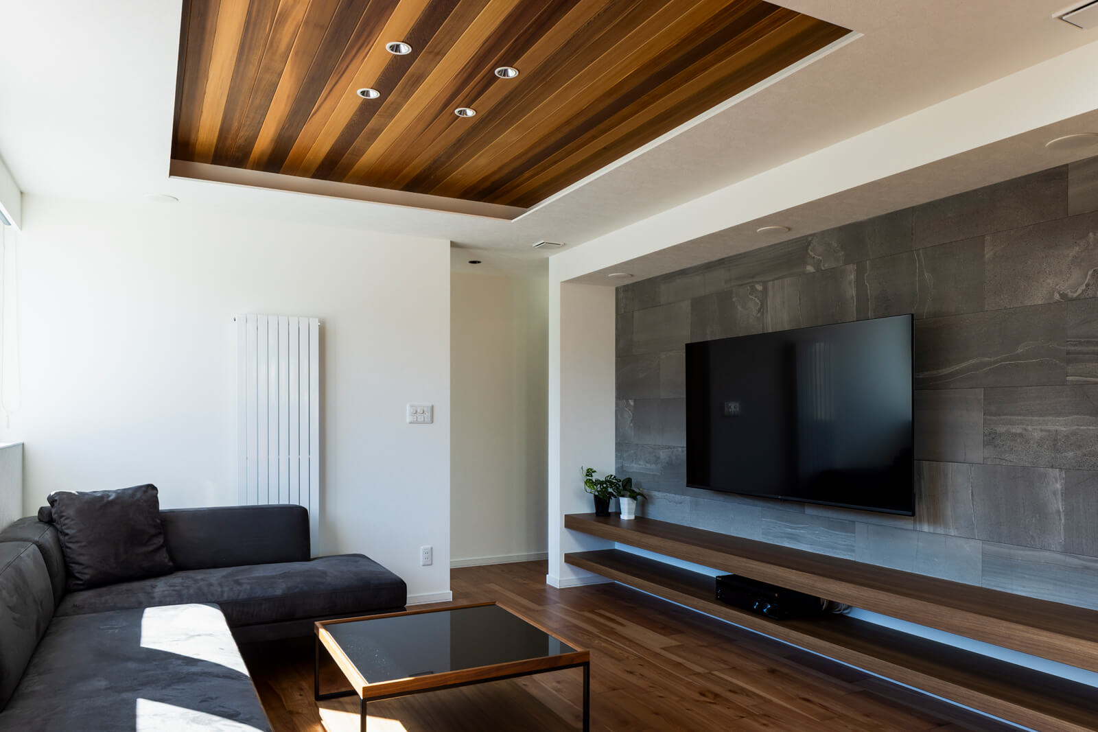 ゆっくりとくつろげる空間を目指したリビングは、天井にはレッドシダーの羽目板を張り、間接照明を造作した。造作テレビ台の壁面には、石材風のエコカラットを張り、5.1chスピーカーを埋め込んでホームシアターに