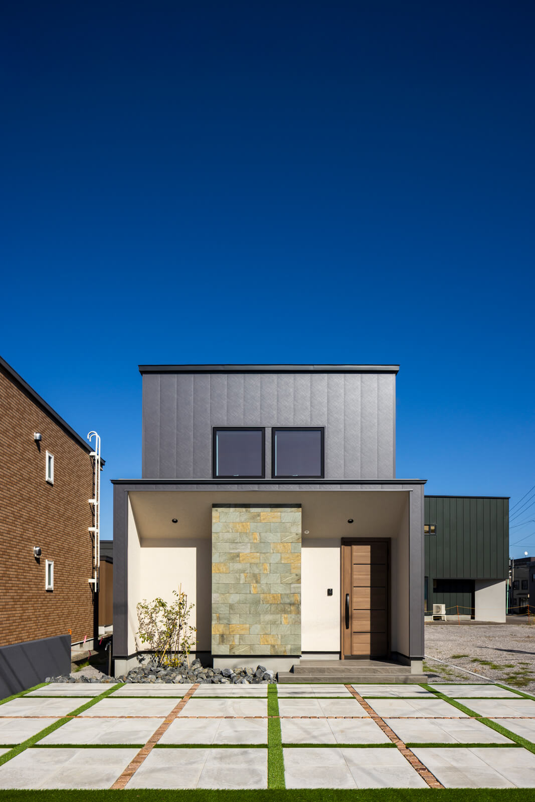 シンプルなフォルムに多彩な表情を加えた外観。駐車スペースにも、コンクリート平板と人工芝、天然石(ピンコロ)を用いて、遊び心あるデザインで仕上げた